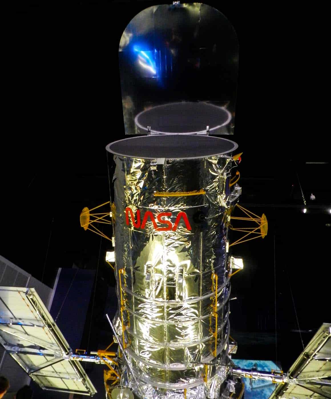 Réplica do Telescópio Espacial Hubble suspenso no teto da exposição Space Shuttle Atlantis, com painéis solares estendidos.