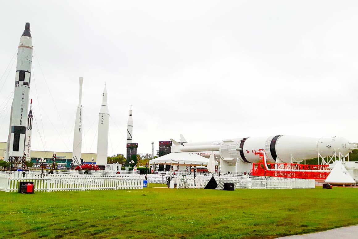 Rocket Garden no Kennedy Space Center: visitantes caminhando entre foguetes históricos da NASA dos programas Mercury, Gemini e Apollo, sob céu nublado em dia chuvoso.