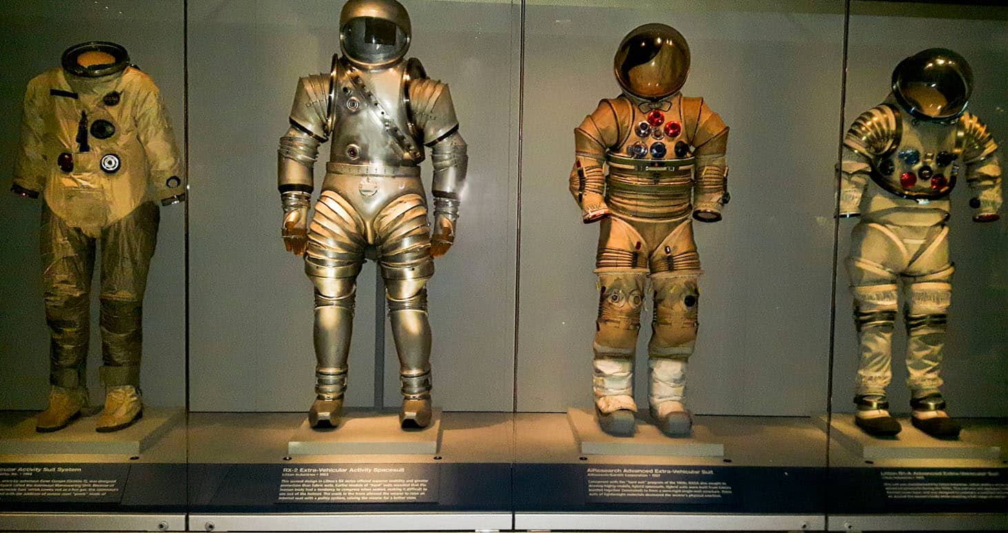 Exibição de trajes espaciais históricos no Kennedy Space Center: vestimentas da NASA dos programas Apollo, Mercury e Gemini, usadas por astronautas em missões espaciais, com capacetes e luvas detalhadas