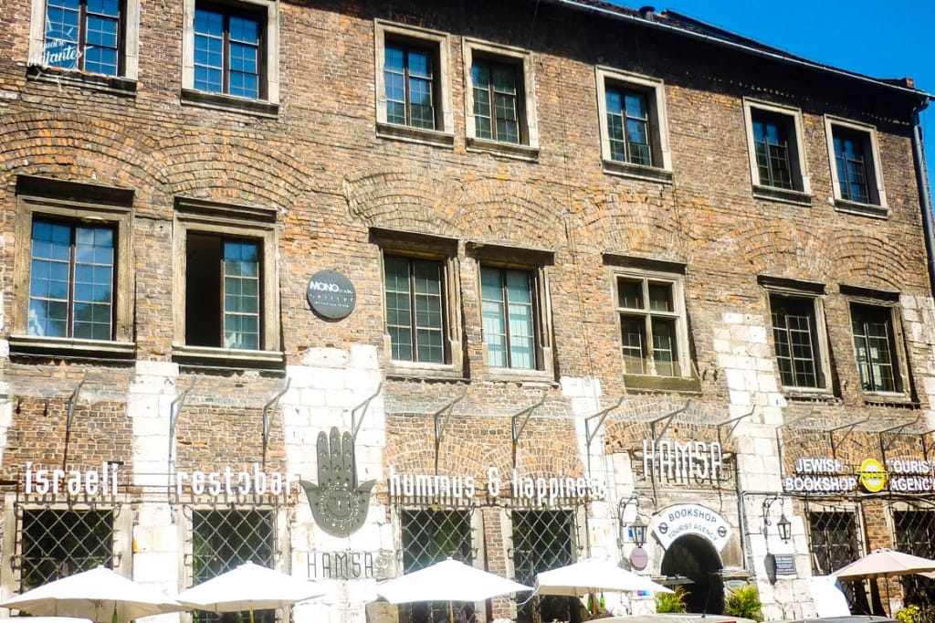 Rua charmosa do Bairro Judeu Kazimierz em Cracóvia, com edifícios históricos coloridos, sinagogas e placas judaicas, atmosfera boêmia revitalizada após filmagens de A Lista de Schindler, mistura perfeita de memória e bares modernos na antiga capital polonesa.