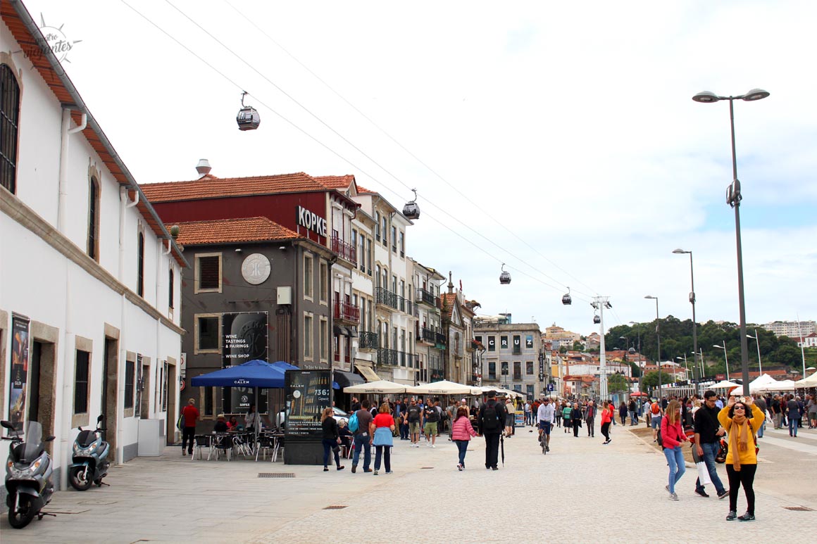 Calçadão à beira do Rio Douro em Vila Nova de Gaia com caves de vinho do Porto, vegetação ribeirinha e céu claro.