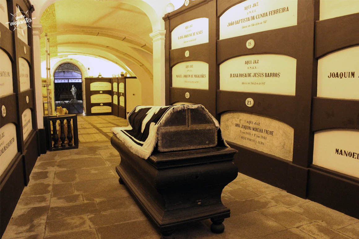 Túnel subterrâneo das catacumbas da Igreja de São Francisco na cidade do Porto, com piso de vidro transparente revelando ossos humanos empilhados abaixo