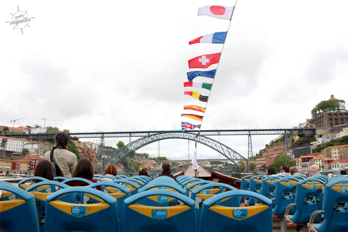 Barco de passeio navegando pelo Rio Douro com Ponte D. Luís I e edifícios coloridos das margens de Porto e Gaia ao fundo