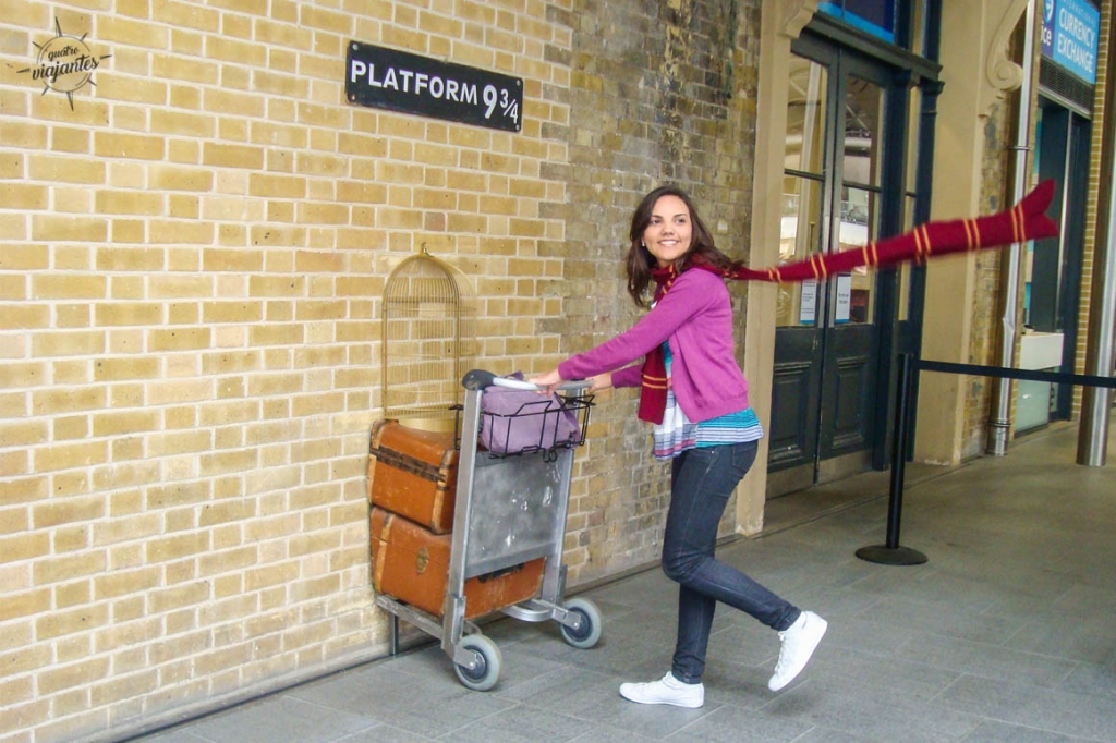 Carrinho de malas atravessando a parede na Plataforma 9 ¾ de King's Cross, Londres, com cicatriz de raio e loja Harry Potter ao fundo.