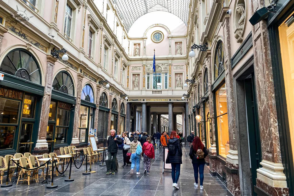 Interior elegante Galeria Royal Saint-Hubert Bruxelas: arco vidro piso mármore, vitrines luxo chocolates joias e pedestres sob teto iluminado neoclássico