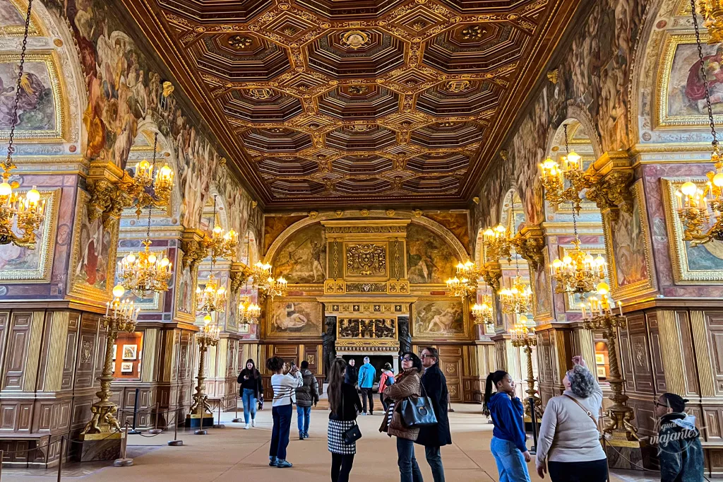 Salão de baile luxuoso do Castelo de Fontainebleau, com pessoas admirando detalhes.