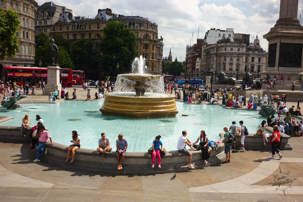 Trafalgar Square em Londres, com a icônica Coluna de Nelson ao centro, fontes e estátuas de leões ao redor, cercada por prédios históricos como a National Gallery.