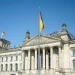 Fachada do Reichstag, o Parlamento Alemão em Berlim, com bandeira alemã hasteada sob céu azul ensolarado