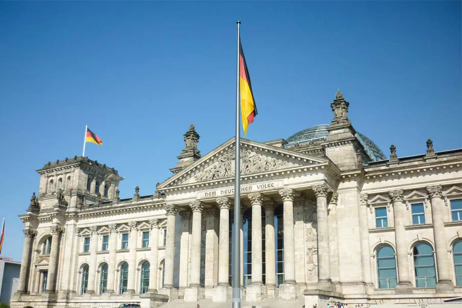 Fachada do Reichstag, o Parlamento Alemão em Berlim, com bandeira alemã hasteada sob céu azul ensolarado