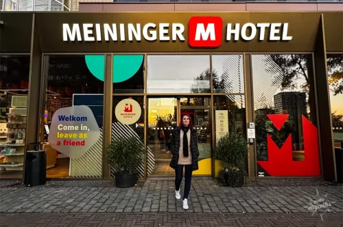 Entrada do Meiniger Hotel Amsterdam ao pôr do sol, fachada moderna com placas "Welkom" e plantas