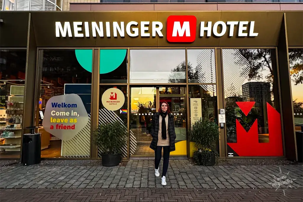 Entrada do Meiniger Hotel Amsterdam ao pôr do sol, fachada moderna com placas "Welkom" e plantas