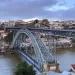 Ponte D. Luís I que liga a cidade do Porto a Vila Nova de Gaia. vista de cima com arco metálico sobre o Rio Douro, edifícios coloridos de Porto e Gaia sob céu parcialmente nublado.