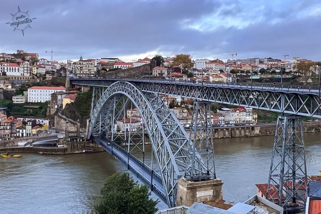 Ponte D. Luís I que liga a cidade do Porto a Vila Nova de Gaia. vista de cima com arco metálico sobre o Rio Douro, edifícios coloridos de Porto e Gaia sob céu parcialmente nublado.