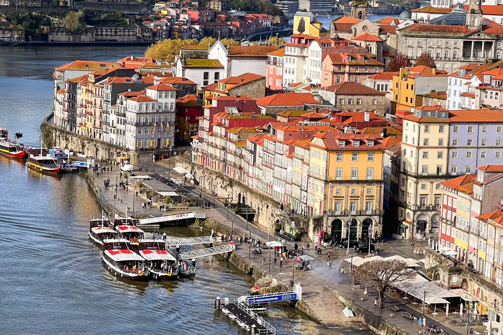 Vista panorâmica da cidade do Porto com Rio Douro, Ponte Luís I, casarões coloridos nas margens e céu azul claro"