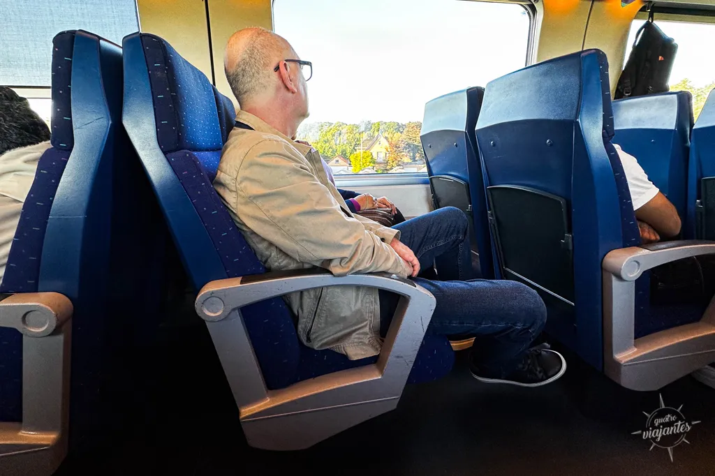 pessoas sentadas em seus assentos de trem de longa distância na Europa, com destaque para o espaço entre as poltronas para acondicionar bagagens