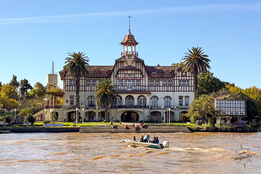 Vista do histórico prédio do Club de Regatas La Marina a partir do Paseo Victorica em Tigre, Argentina, com um barco navegando pelo rio em um dia ensolarado.
