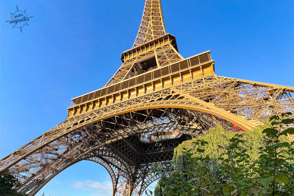 Torre Eiffel em foto tirada por baixo, em dia de céu claro.